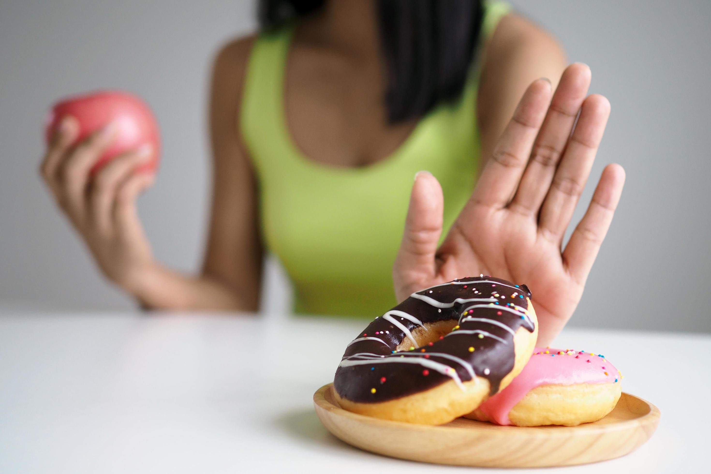 Women push the donut plate that is a mixture of trans fat. And choose to hold the apple. Don’t eat junk food. diet concept Stock Free