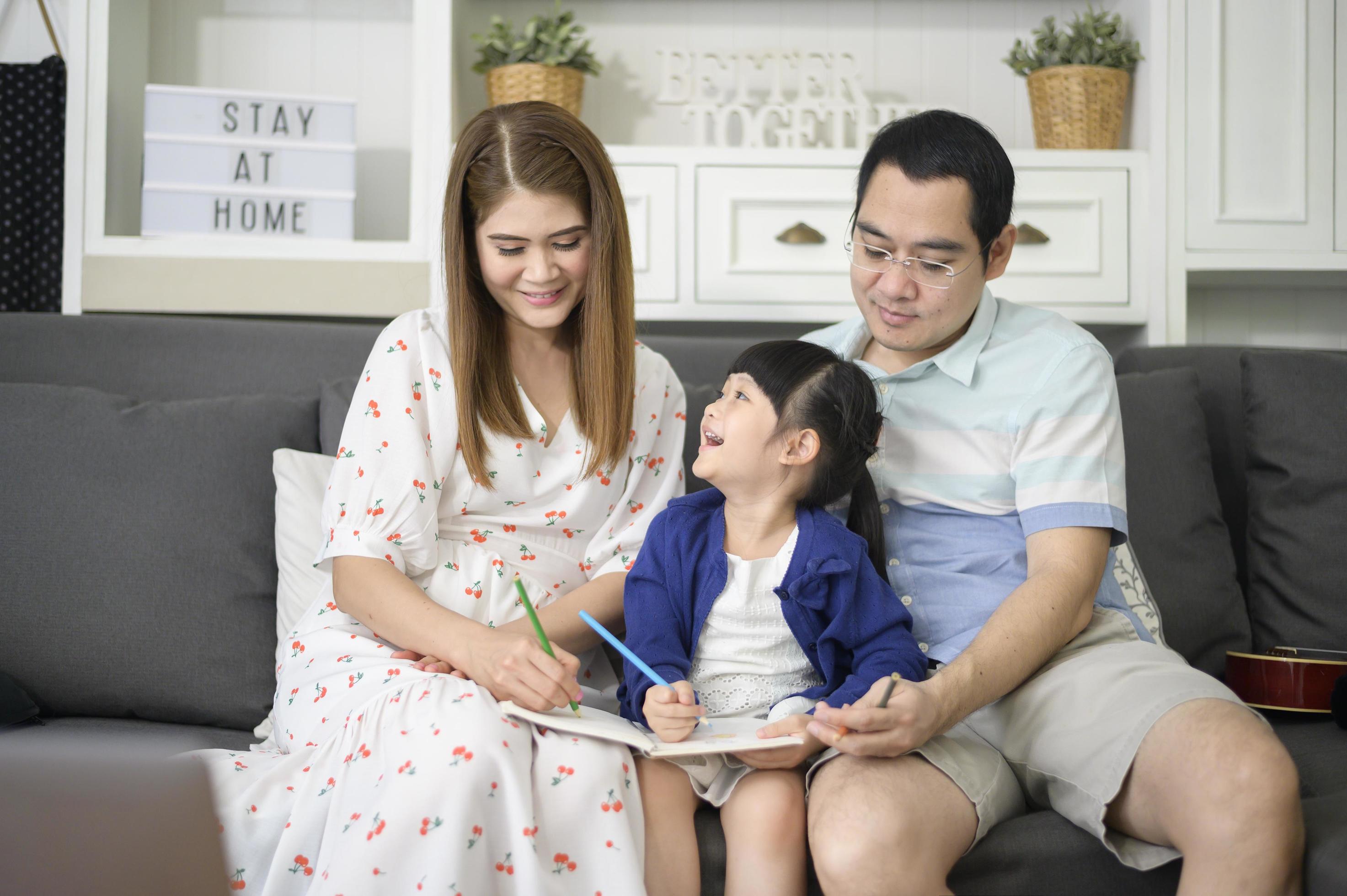 Happy asian parent teaching little cute daughter to do homework and drawing picture together at home. Stock Free