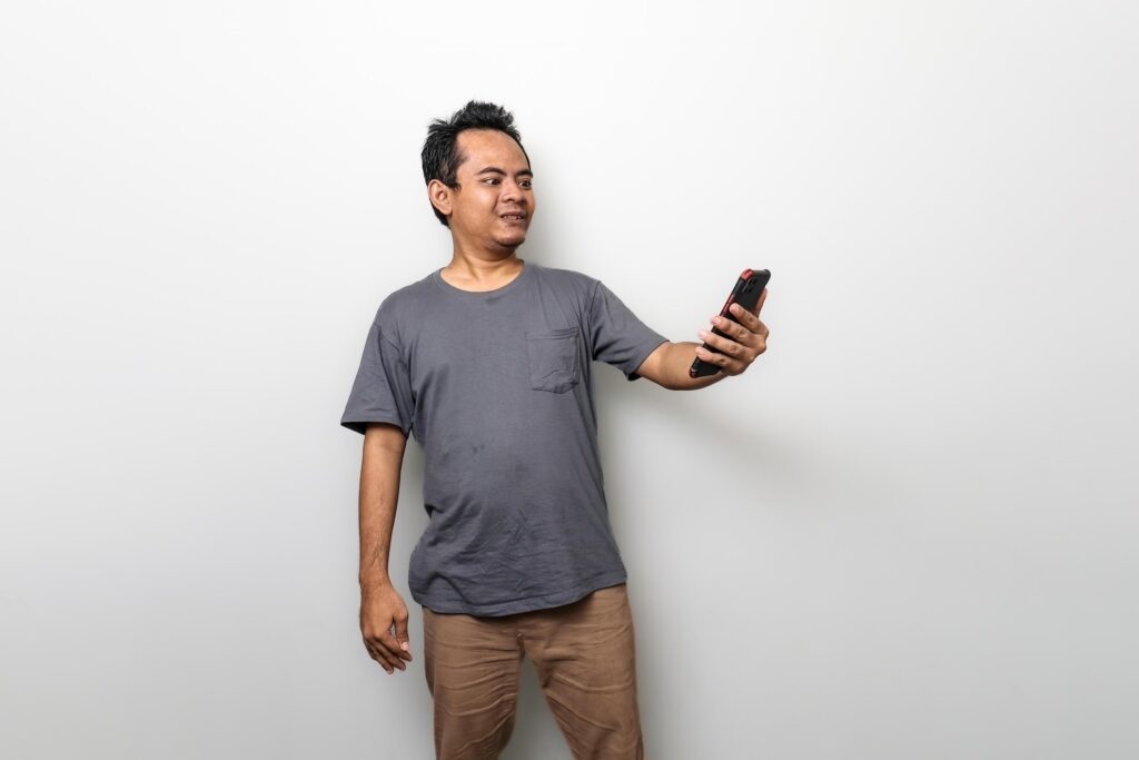 an asian man in gray is surprised when he looks at a smartphone isolated on white background Stock Free