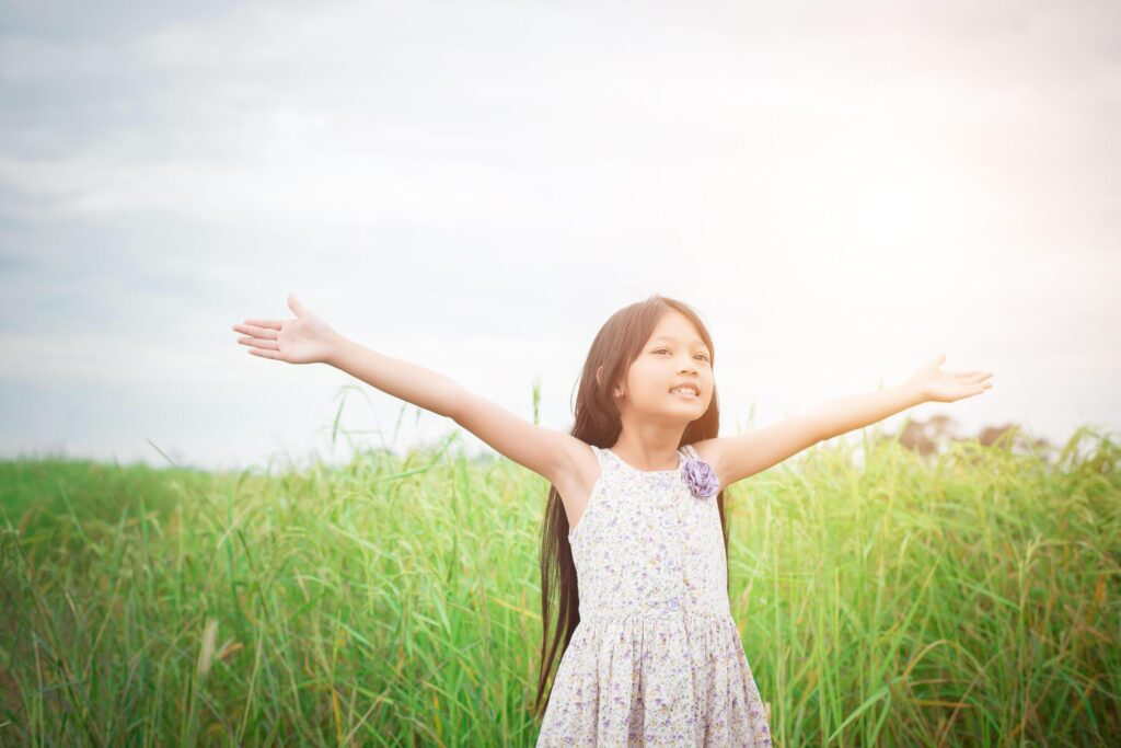 Little cute asian girl standing among the purple flower field sunshine day. Freedom enjoying with nature. Stock Free