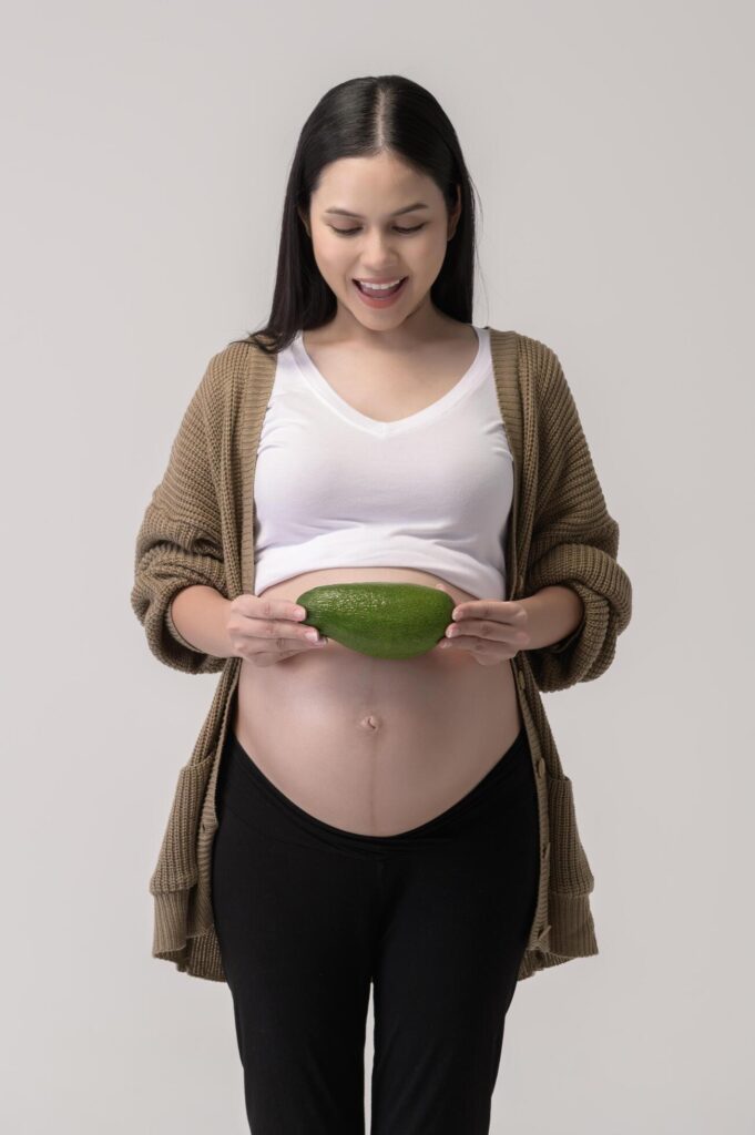 Portrait of Beautiful pregnant woman holding avocado over white background studio, health and maternity concept Stock Free