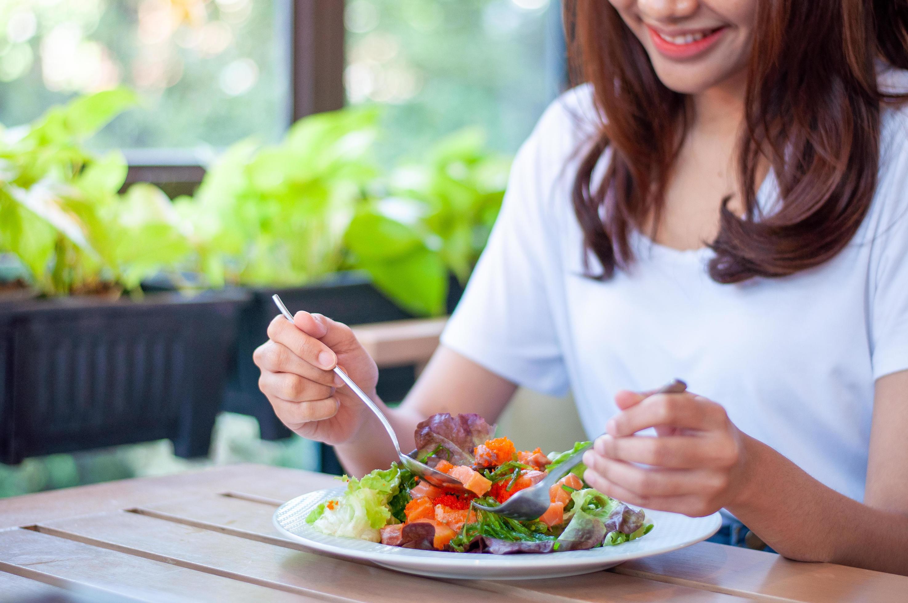 The smiling woman enjoys eating a salmon salad. To lose weight and diet, eat foods that are beneficial to the body. Weight loss concept. Stock Free