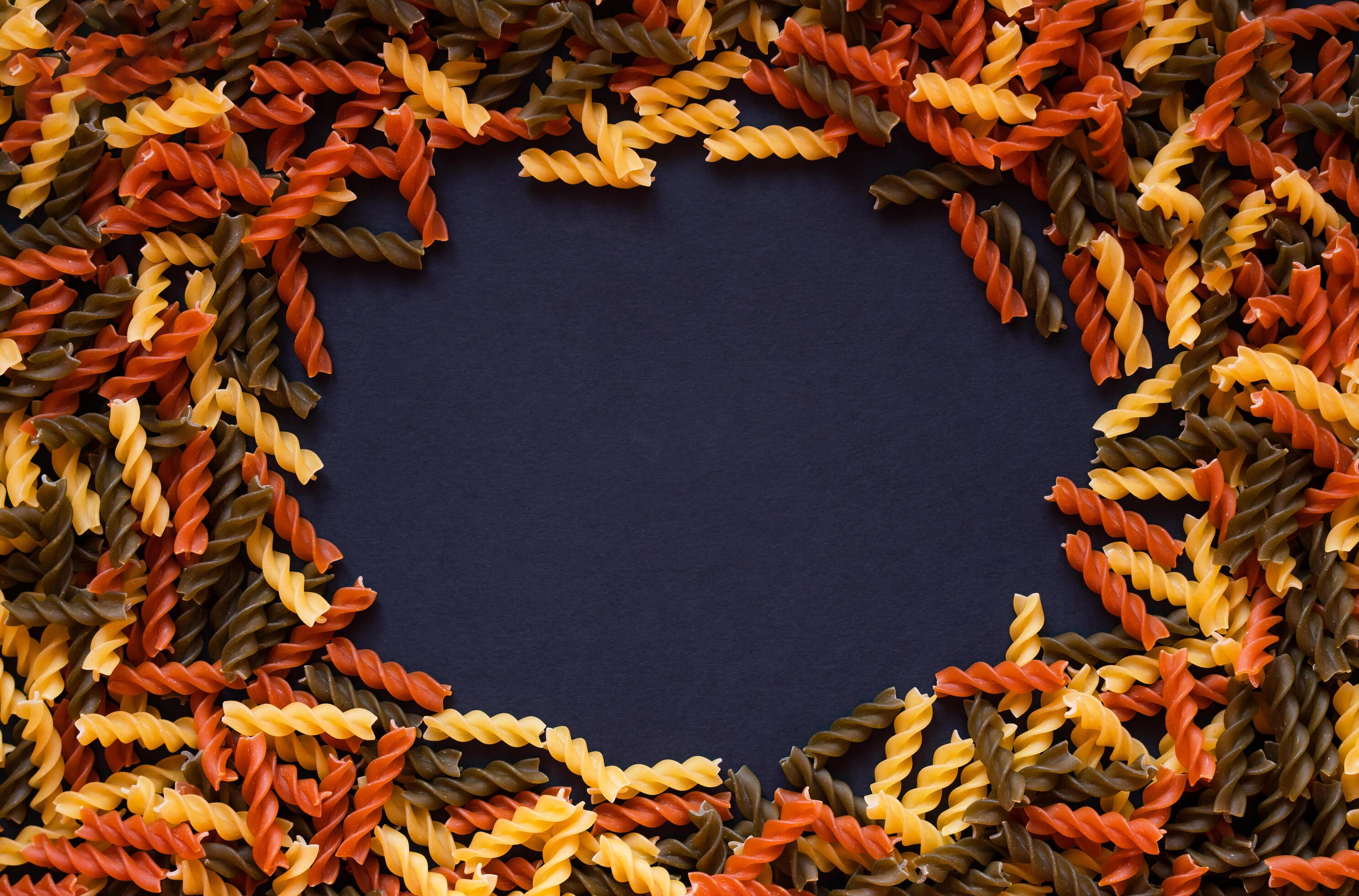 Italian tricolor fusilli paste scattered in the form of a frame on a black background. Top view. Copy space. Selective focus. Stock Free