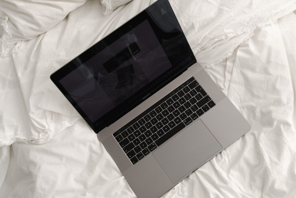 Working with a laptop in bed – white cotton bedding Stock Free