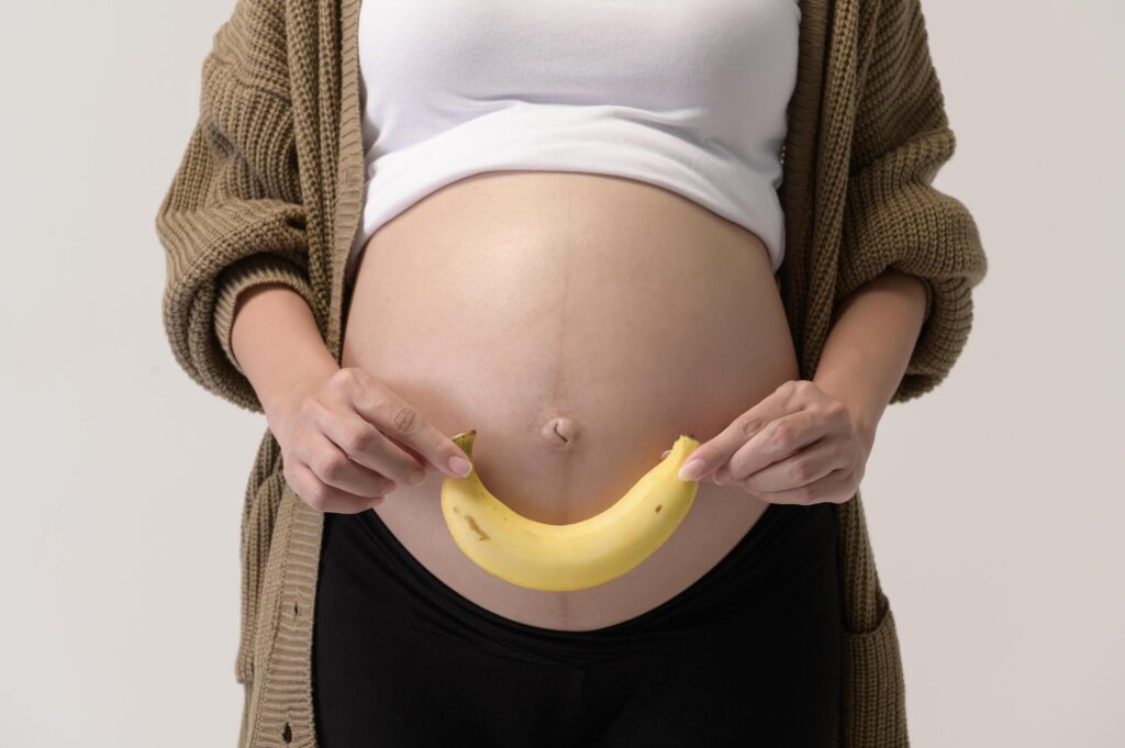 Portrait of Beautiful pregnant woman holding banana over white background studio, health and maternity concept Stock Free