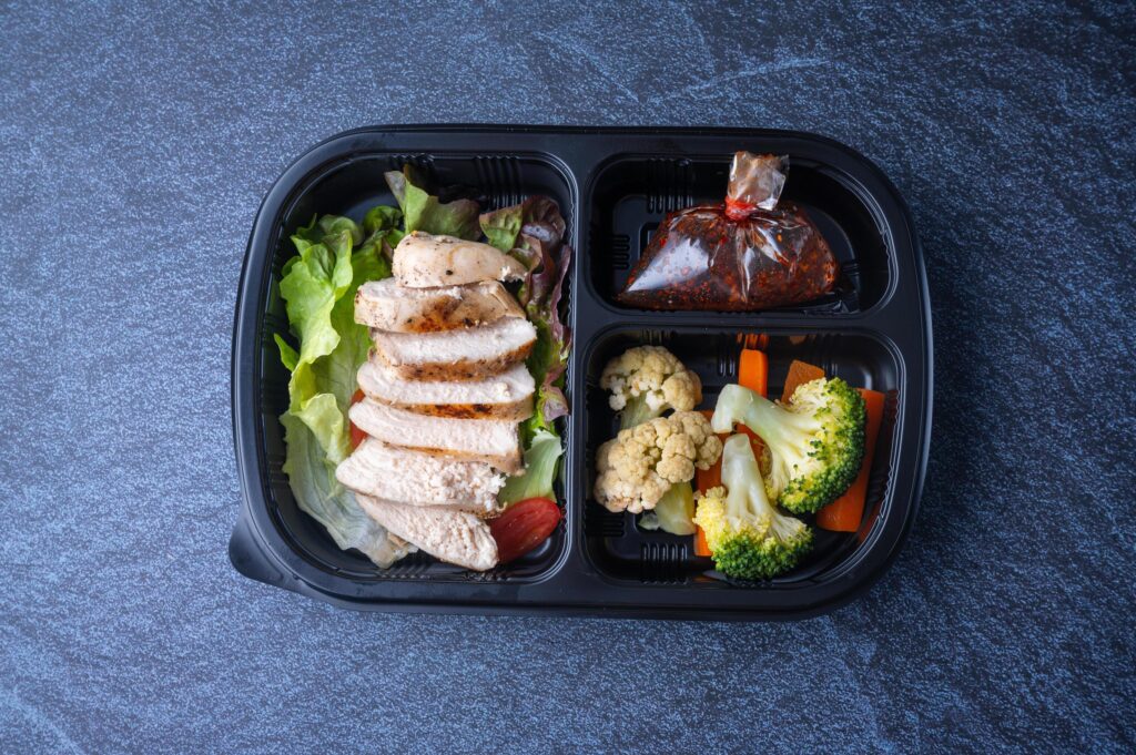 Sectioned plastic food container with sliced chicken salad, broccoli, carrots, and cabbage Stock Free