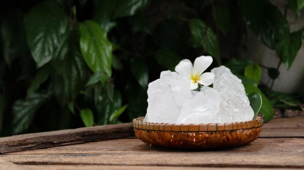 A basket filled with white alum crystals sits on a vibrant green shrub background. Stock Free