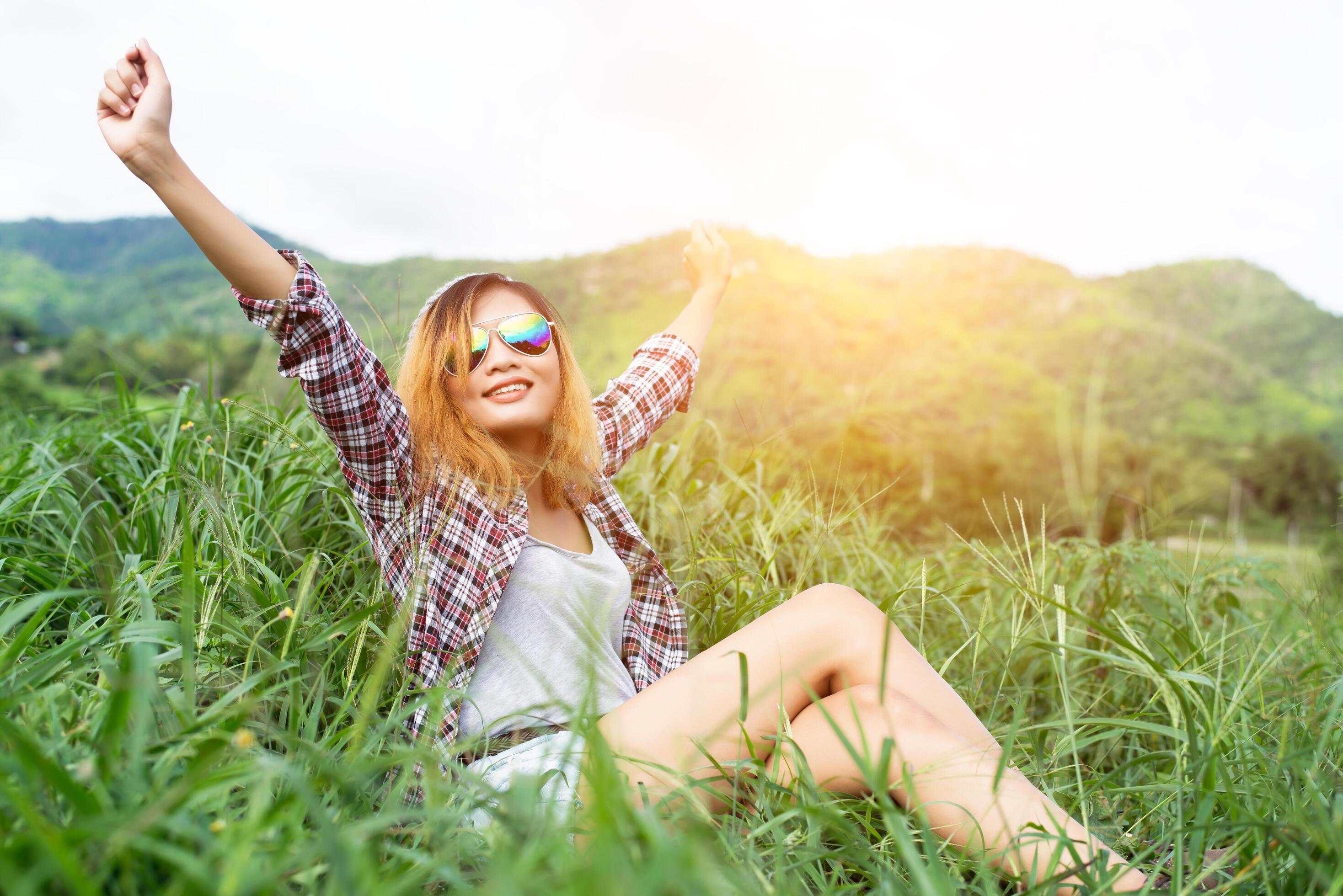 Beautiful hipster woman sitting in a meadow with nature and mountains in the background. Stock Free