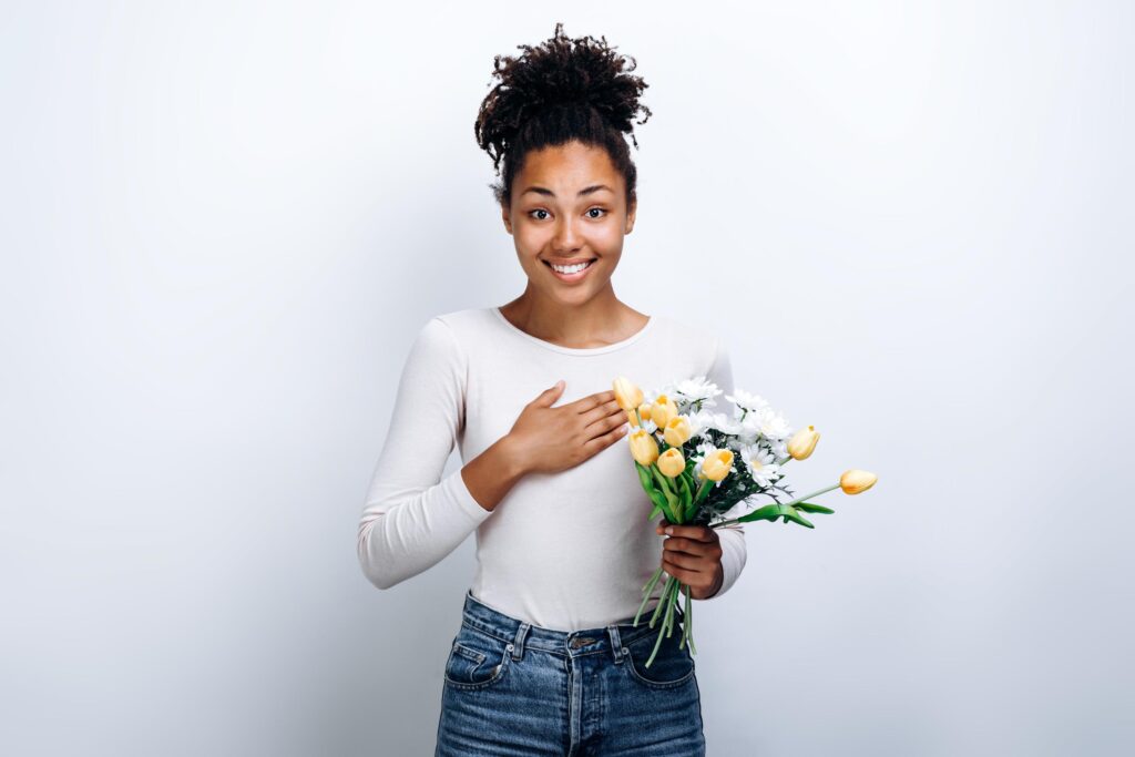 Surprised girl holding a bouquet of beautiful flowers in her hands on a white wall background Stock Free