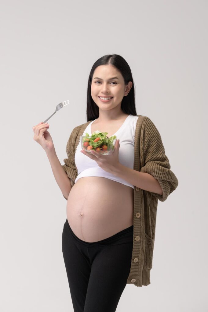 Portrait of Beautiful pregnant woman eating salad over white background studio, health and maternity concept Stock Free