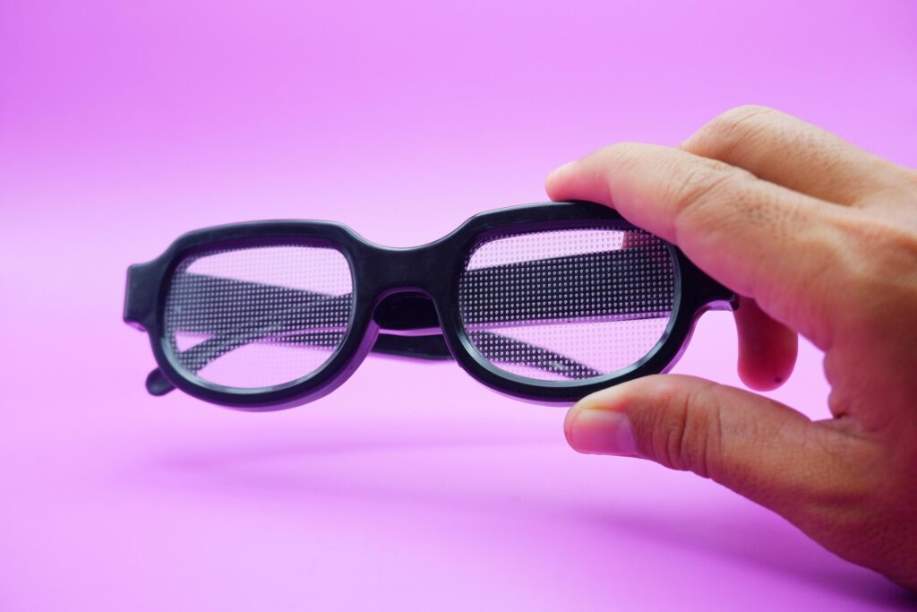 hand holding black frame glasses. black frame glasses isolated on purple background. black frame glasses with curved frames and transparent glass. Stock Free