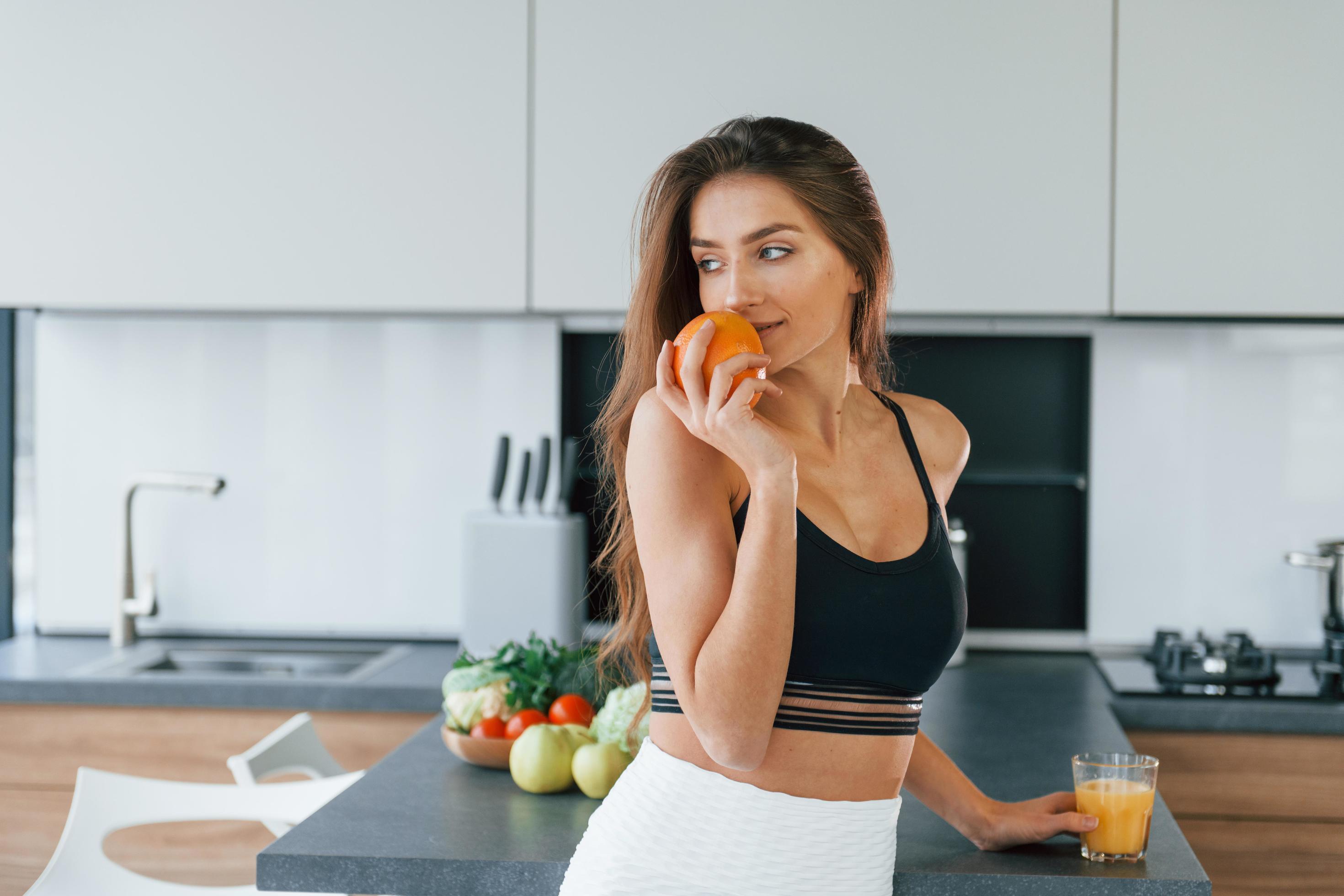 Fresh orange. Young european woman is indoors at kitchen indoors with healthy food Stock Free