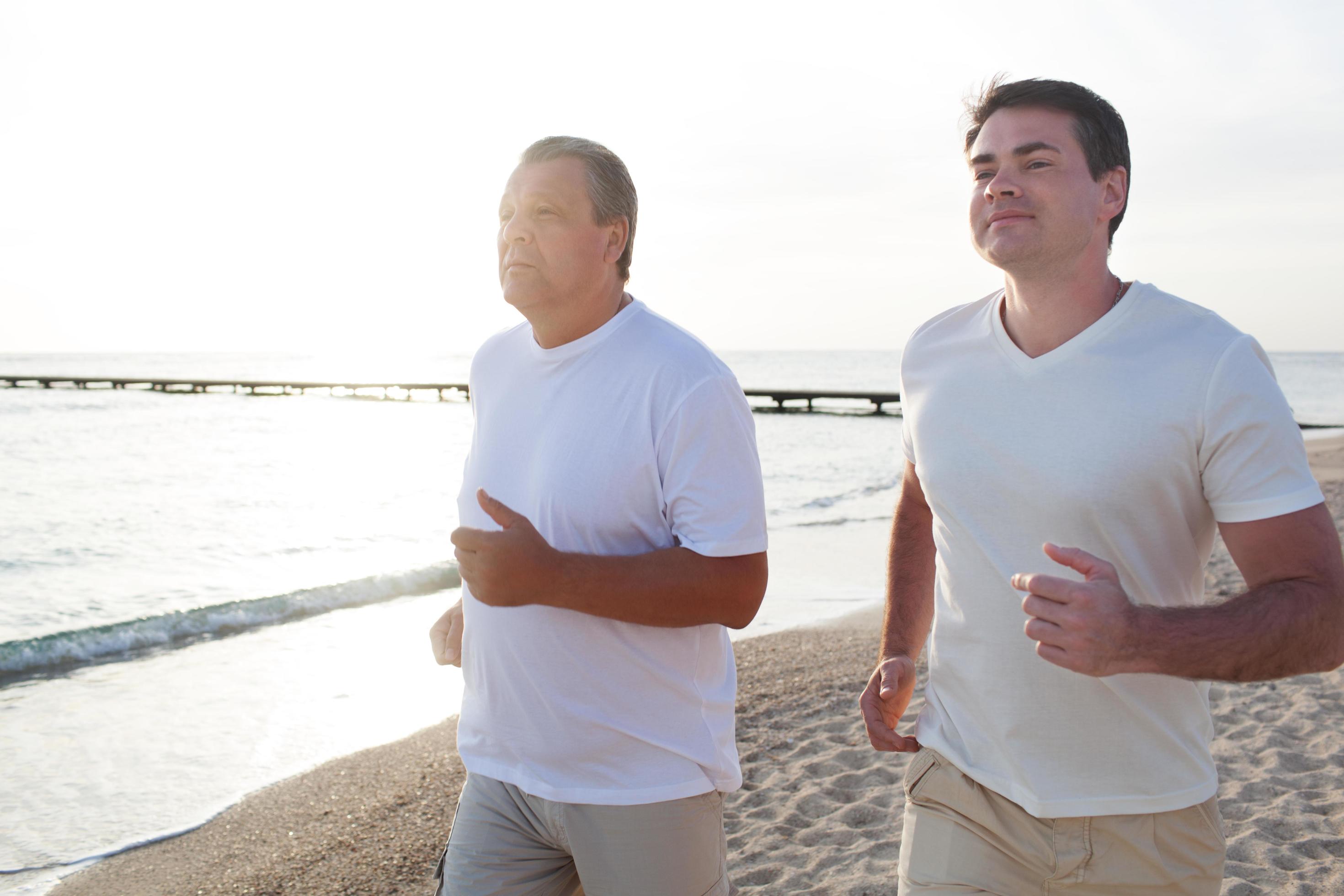 Two men running along the coast in bright sunlight Stock Free