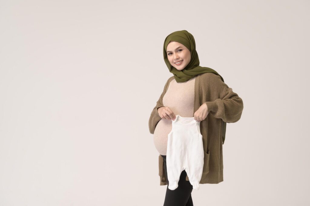 Portrait of Pregnant muslim woman in hijab holding baby cloth over white background studio Stock Free