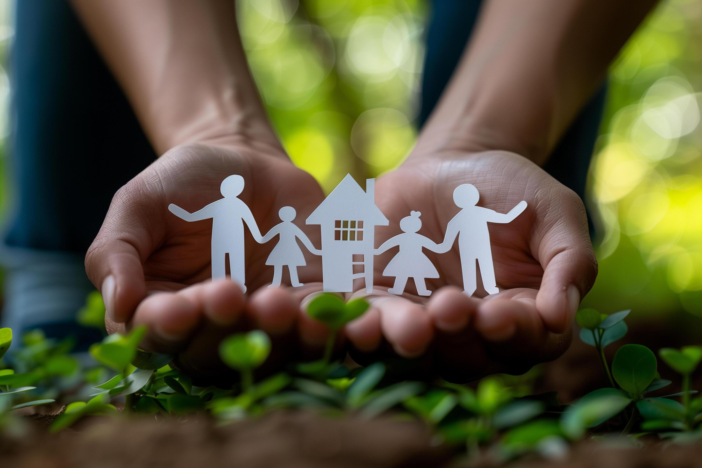 A person holds a paper cut-out of a family and house against a garden. Stock Free