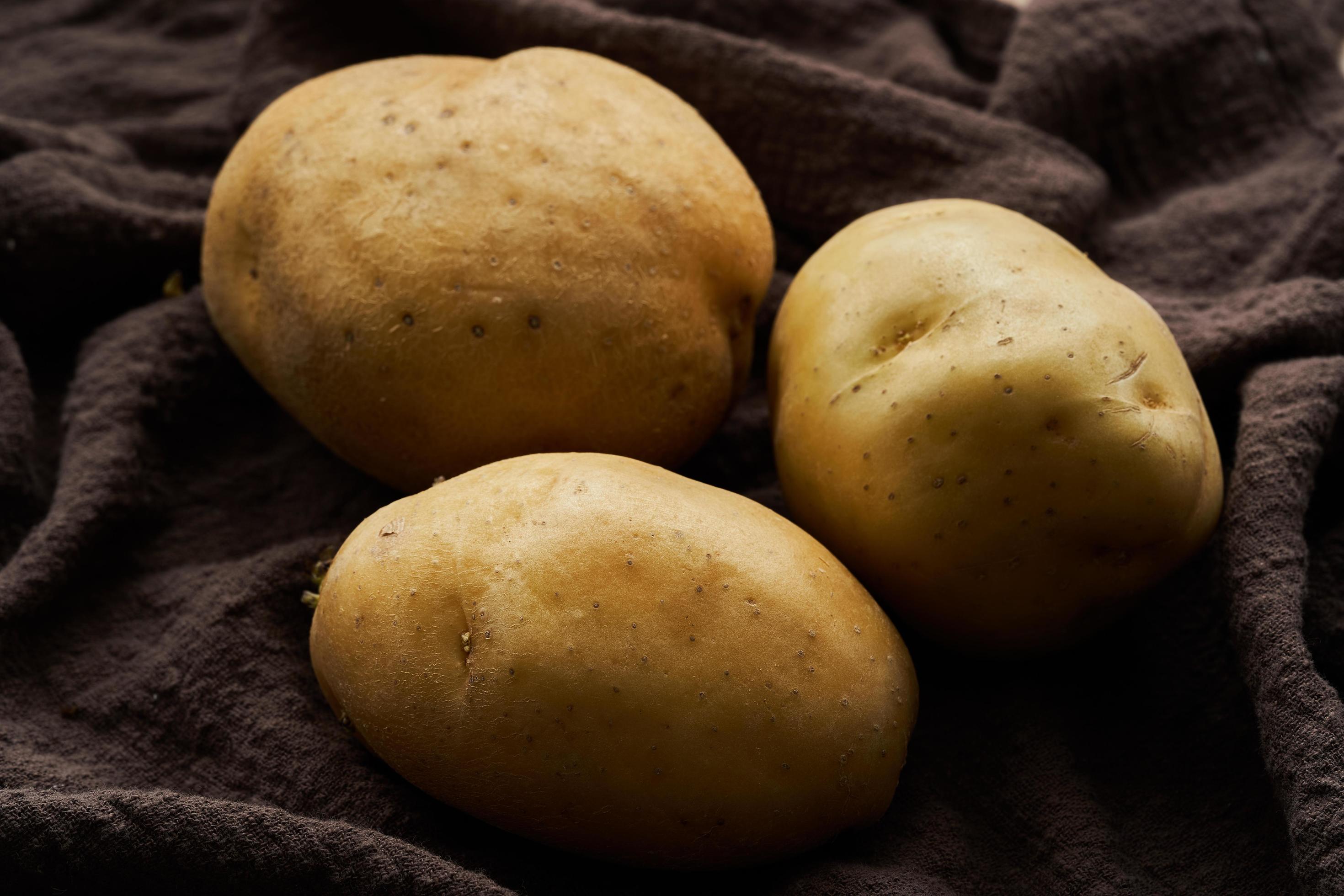 close up raw three potato on brown fabric. food concept background Stock Free