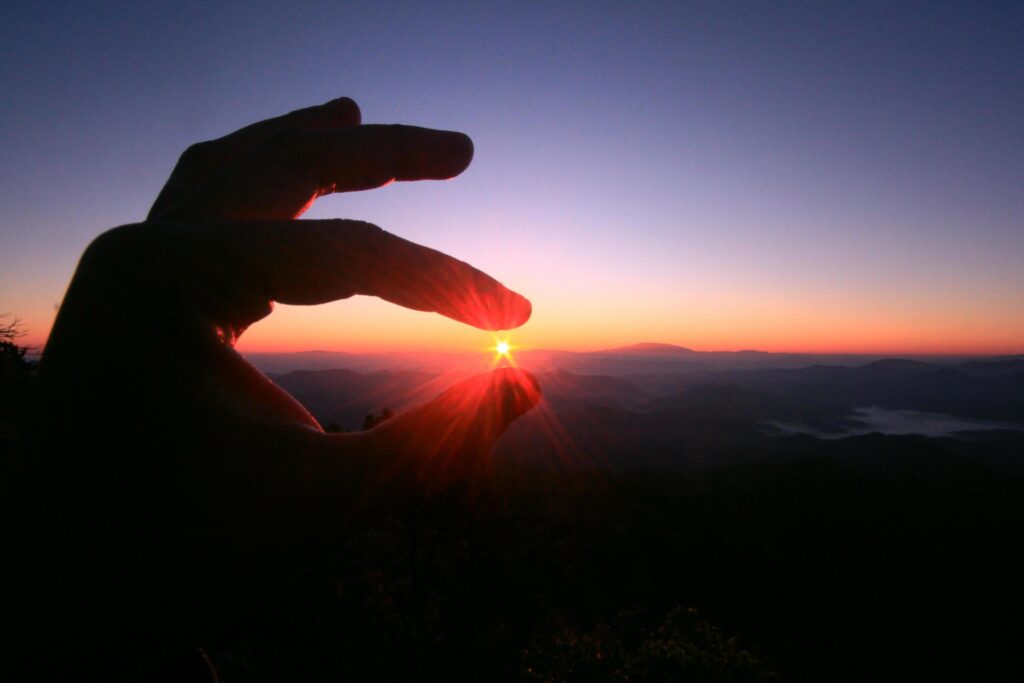 Woman fingers pick beautiful sun in natural twilight of sunset on the mountain Stock Free