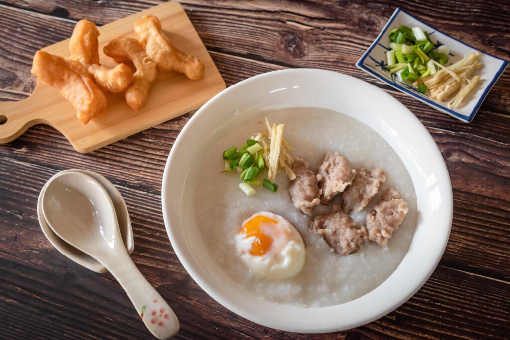 Top view of Chinese rice porridge, Congee with pork, egg and vegetable on wooden background Stock Free