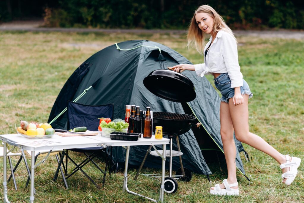 Woman preparing food on barbecue outdoor in the camping and looking at the camera Stock Free