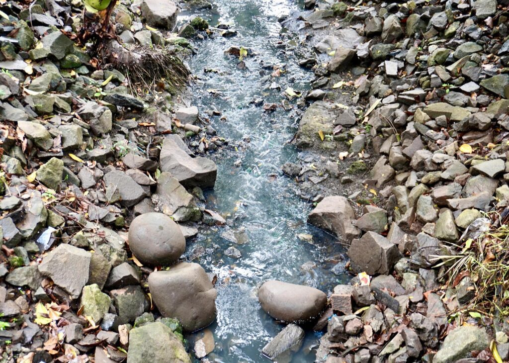 Narrow rough water stream flow between rock stones and pebbles isolated on horizontal ratio background on outdoor environment background photography. Stock Free