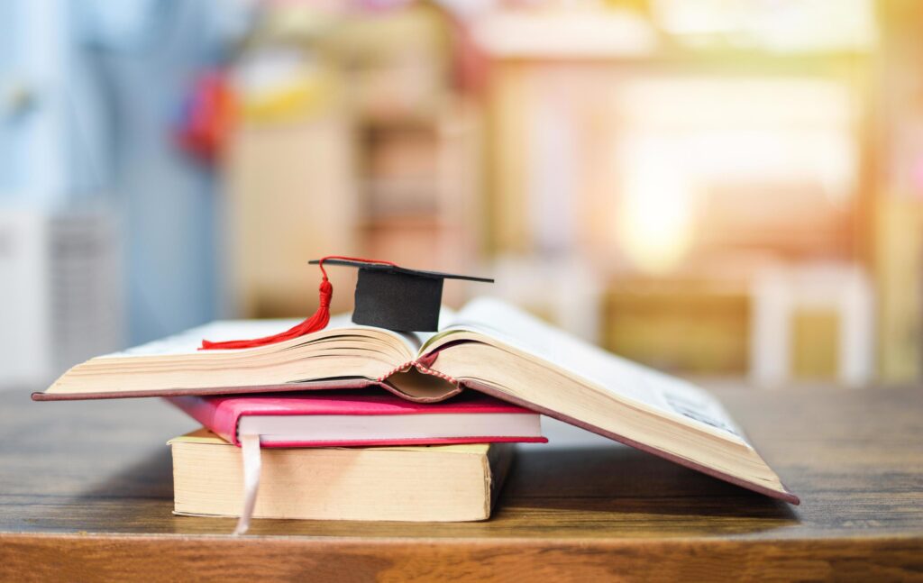 Education concept with graduation cap on a book on the wooden table Stock Free