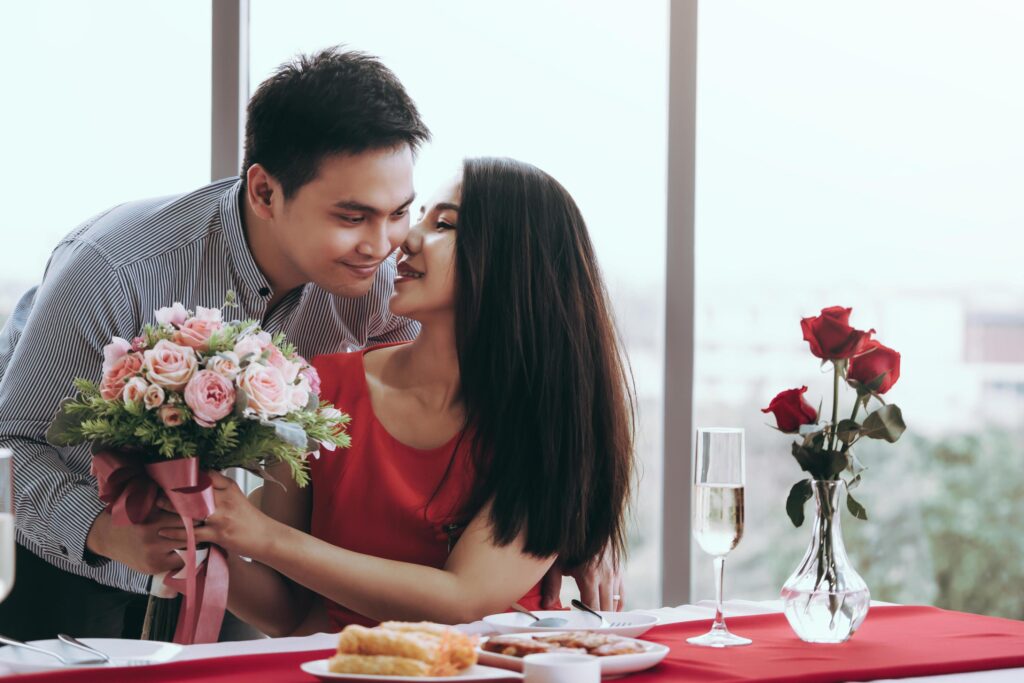 Asian couple with flower bouquet at dinner table on valentine. Stock Free