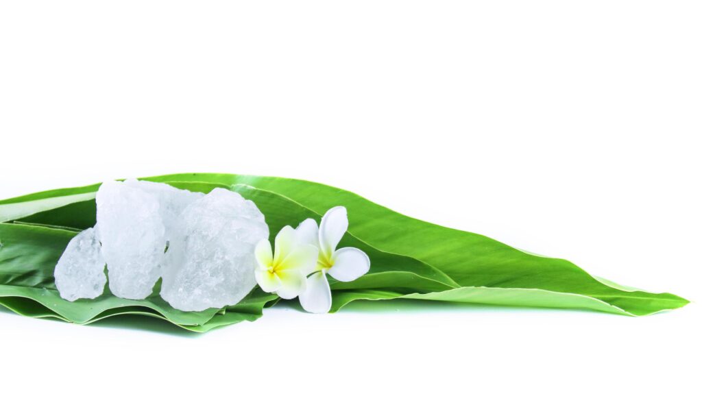 White crystal clear alum cube on green leaf isolated on white background. Stock Free