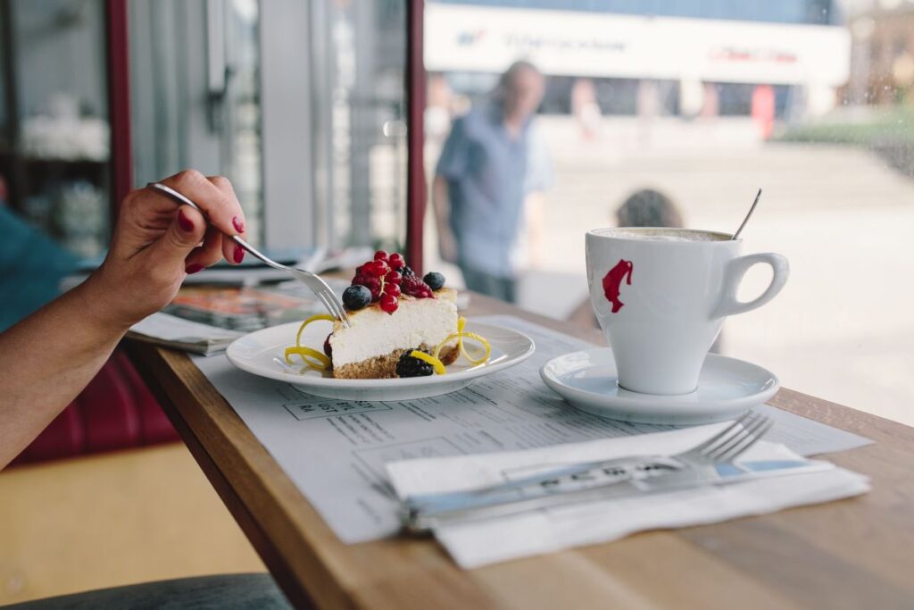 Woman Enjoying Cheese Cake and a Coffee with Fruits in a Cafeteria Stock Free