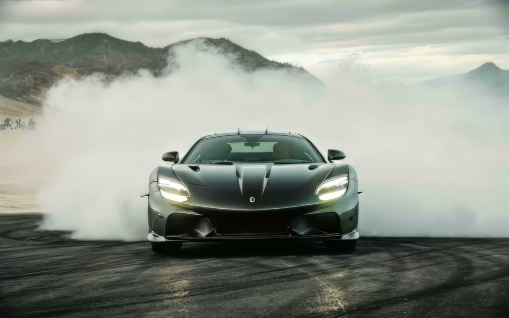 A matte black supercar emerges from a swirling fog bank, its sleek silhouette outlined against a dramatic mountain backdrop. Free Photo