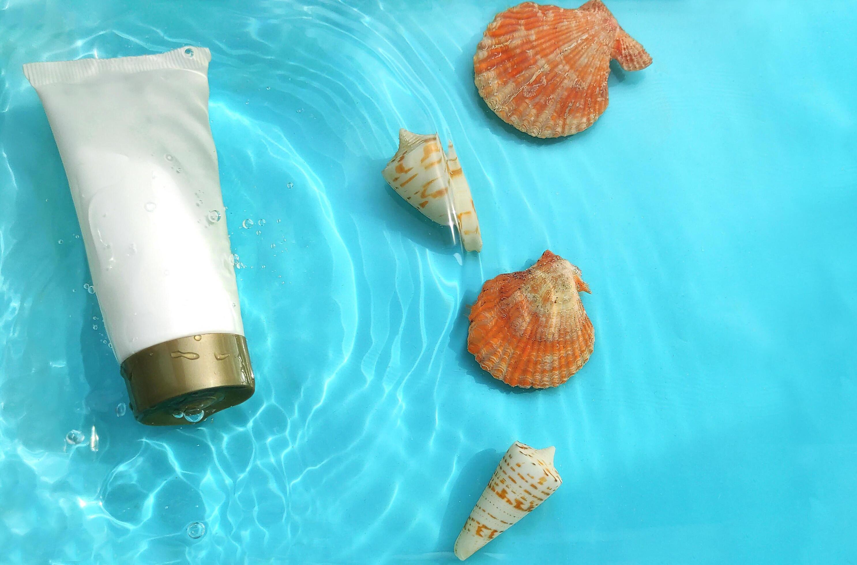 cosmetic product mockup with various seashells in water with water ripples on a blue background. Stock Free