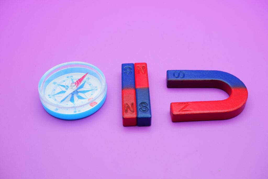 a compass, 2 bar magnets, and a horseshoe magnet isolated on a purple background Stock Free