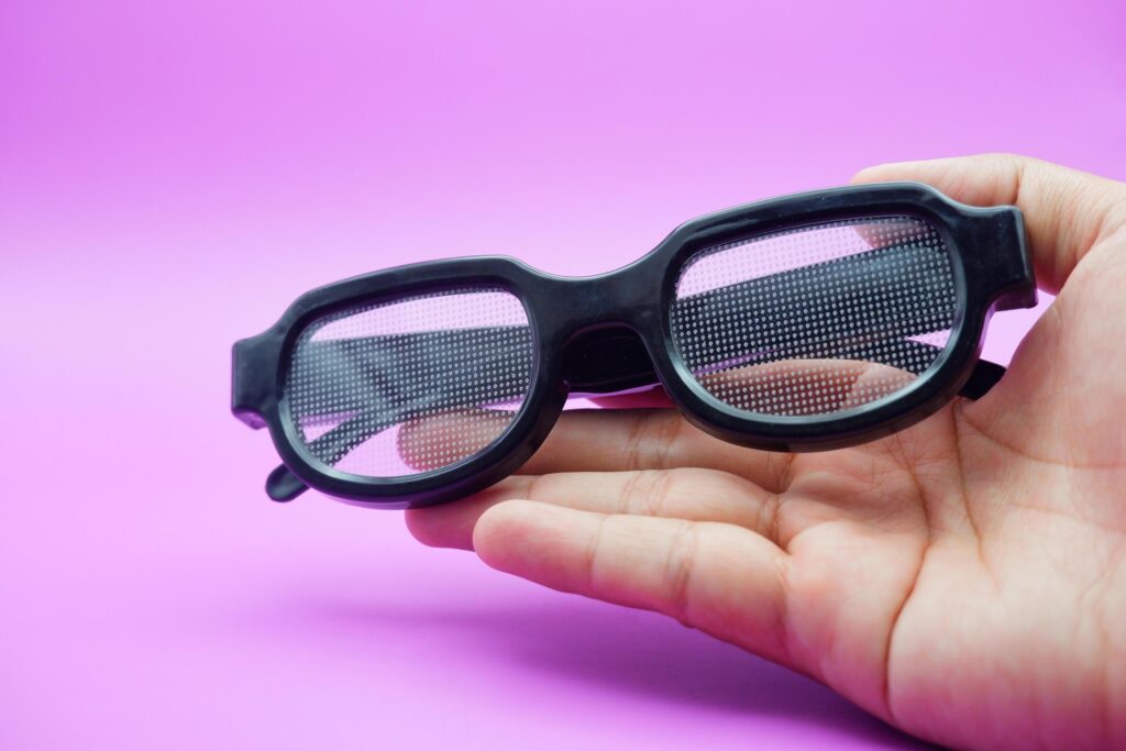 hand holding black frame glasses. black frame glasses isolated on purple background. black frame glasses with curved frames and transparent glass. Stock Free