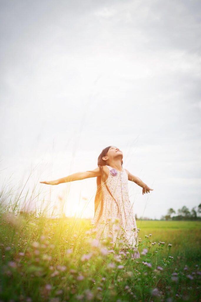 Little cute asian girl standing among the purple flower field sunshine day. Freedom enjoying with nature. Stock Free