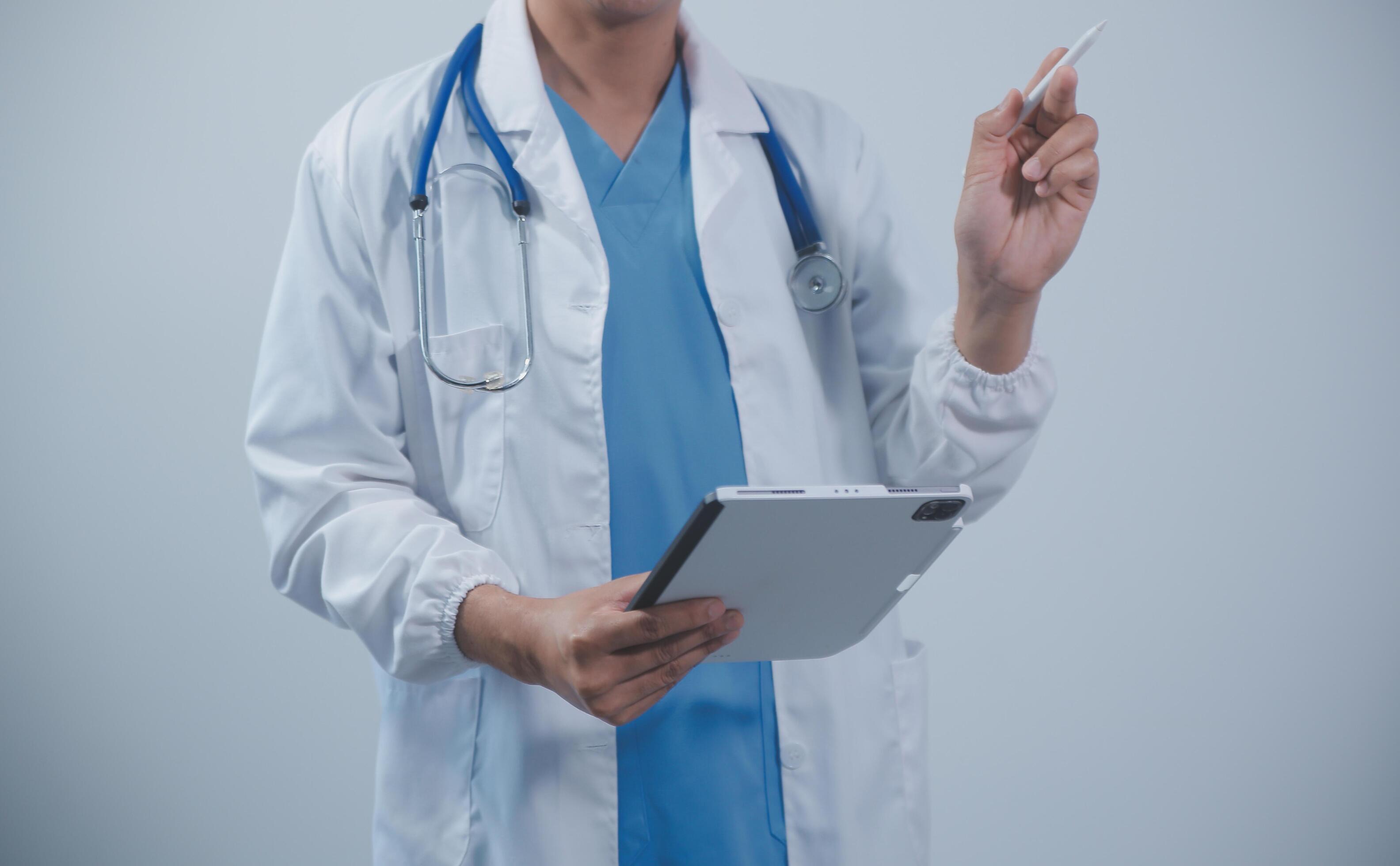 Mature male doctor with tablet pc is giving presentation. Blurred background indoors. Stock Free