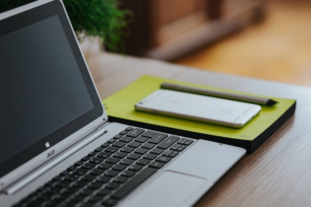 
									Silver Acer laptop, a white Apple iPhone and a notepad on a wooden desk Stock Free