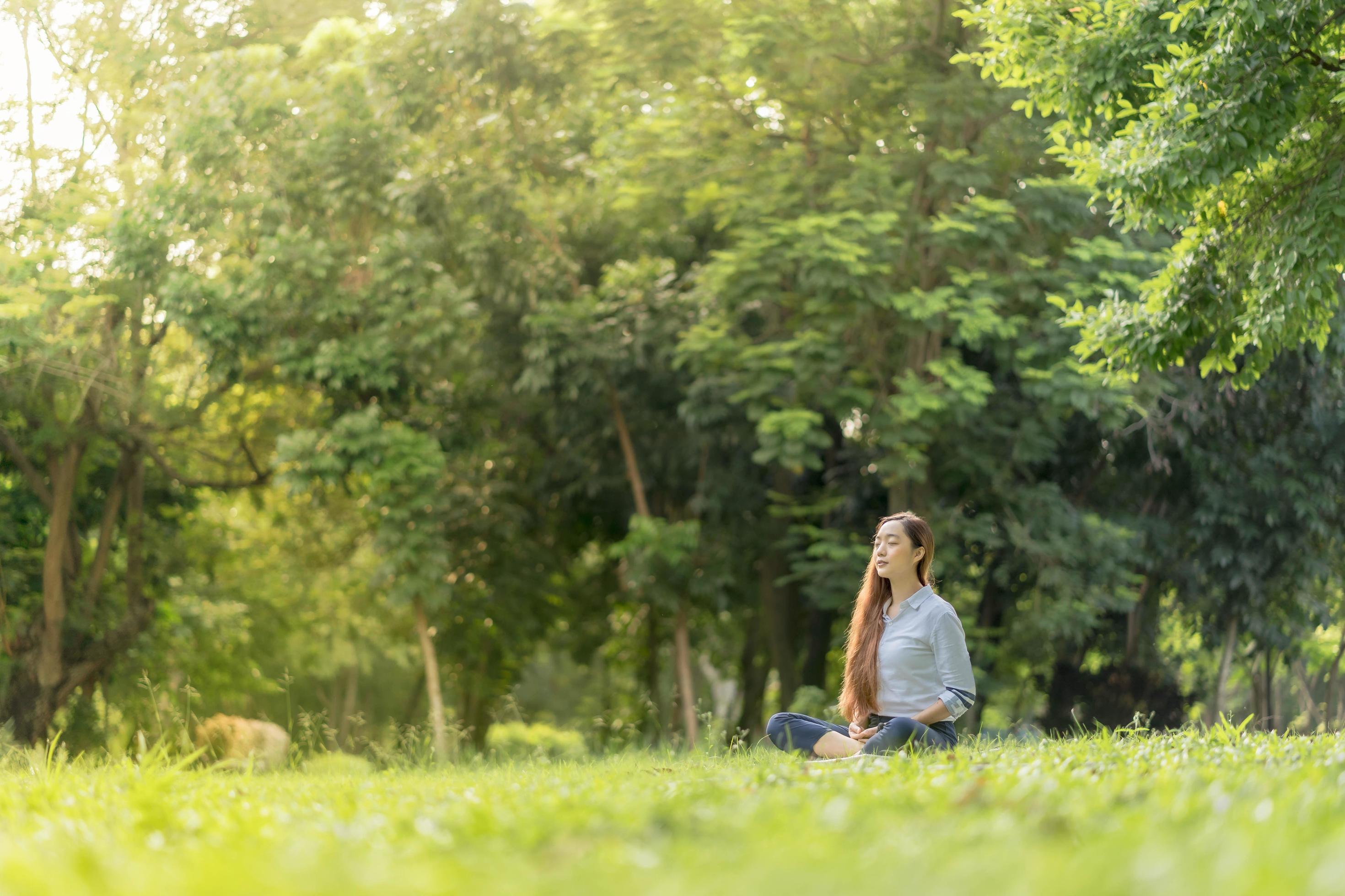 Happy woman doing meditation and relaxing in the park. Meditation in nature. Concept of healthy lifestyle and relaxation. Stock Free