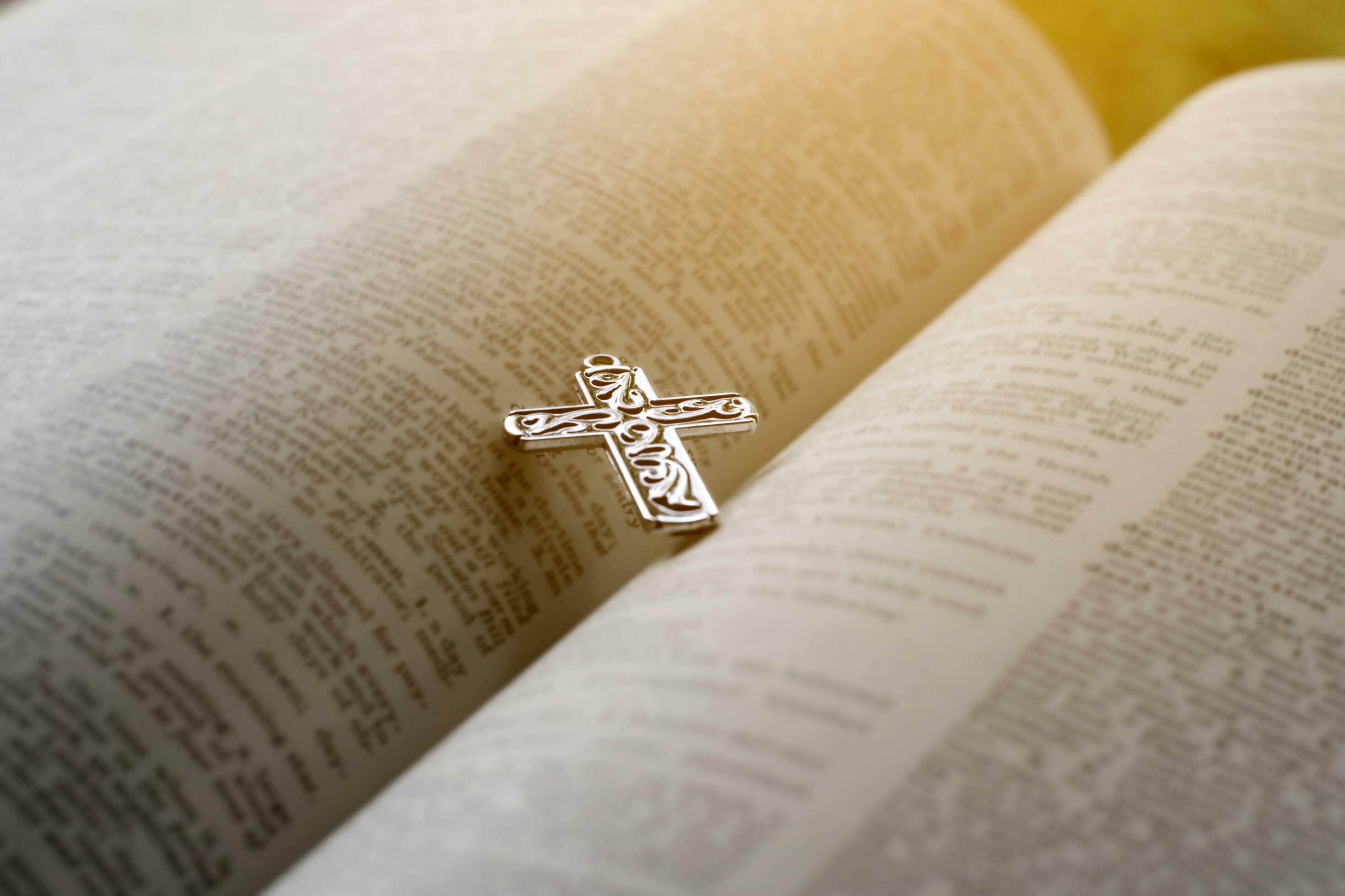 Closeup image of metal cross which places on opending bible book, soft focus, concept for religious lifestyle of christian people around the world. Stock Free