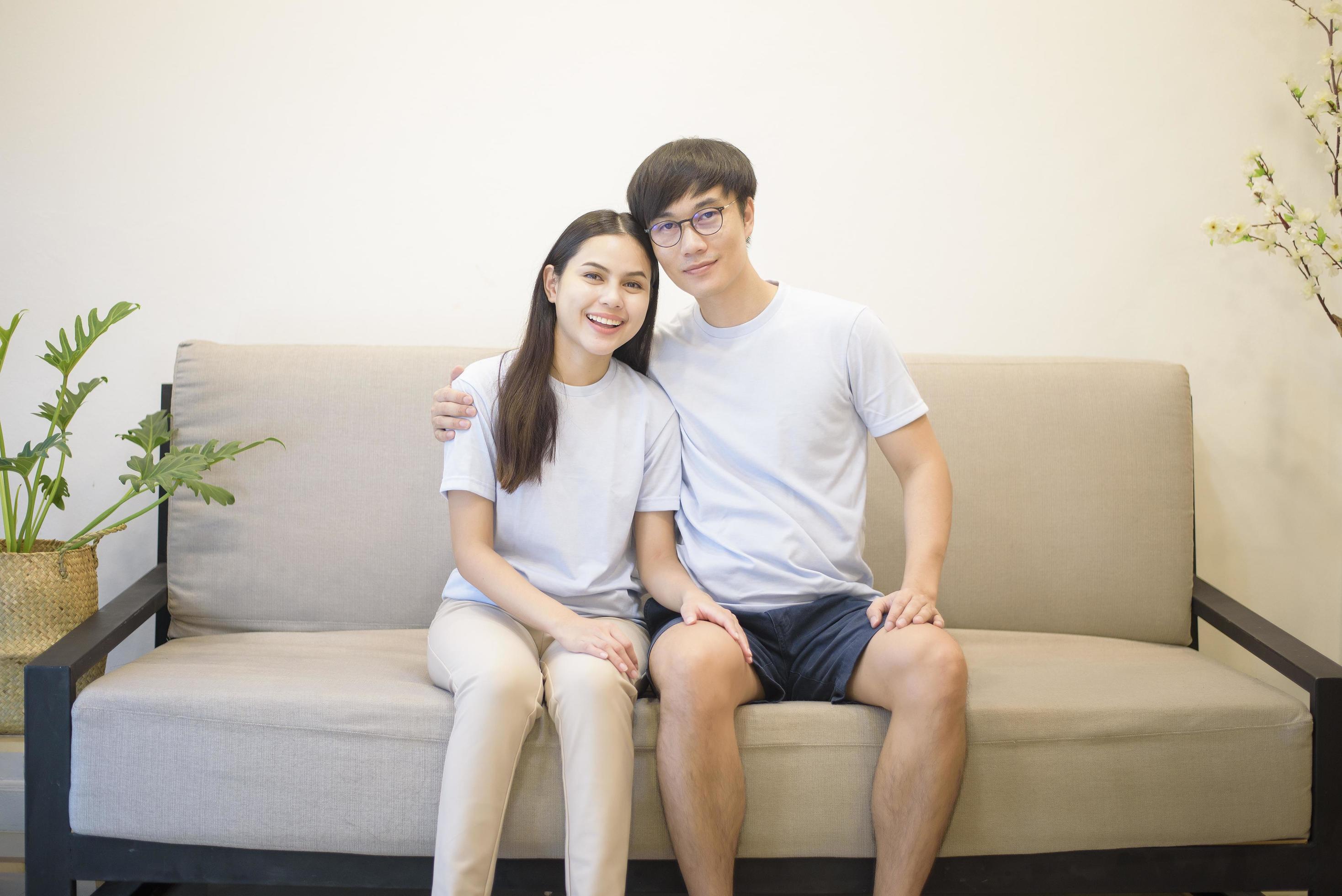 a happy couple wearing blue shirt is sitting on a sofa at home Stock Free