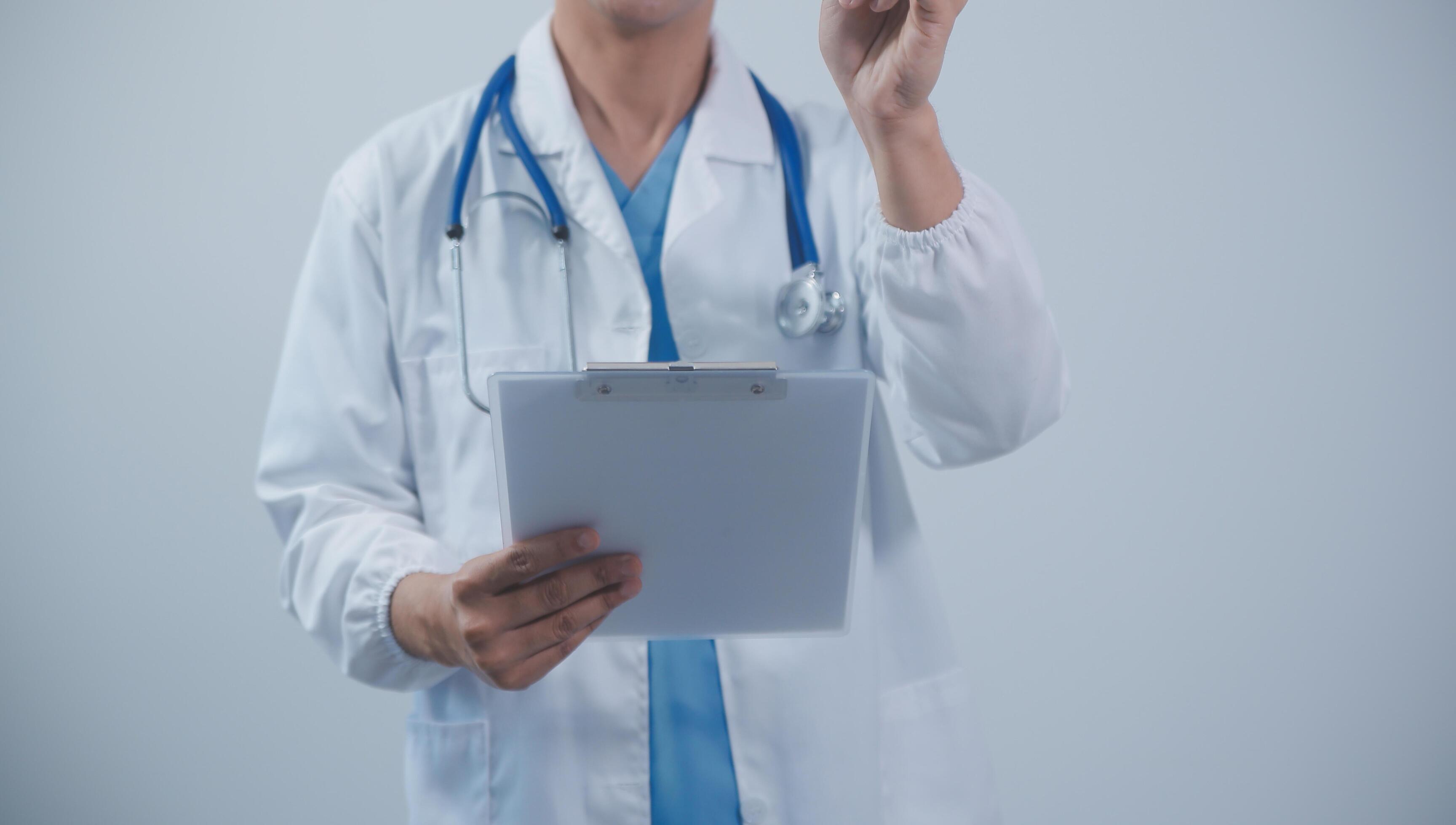 Mature male doctor with tablet pc is giving presentation. Blurred background indoors. Stock Free