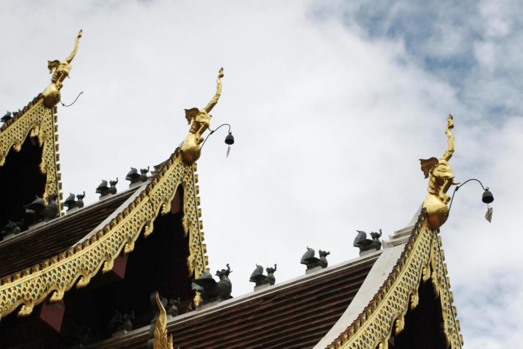 Golden naga and bells hanging on Art Roof of Buddhist temple with blue sky in Thailand Stock Free