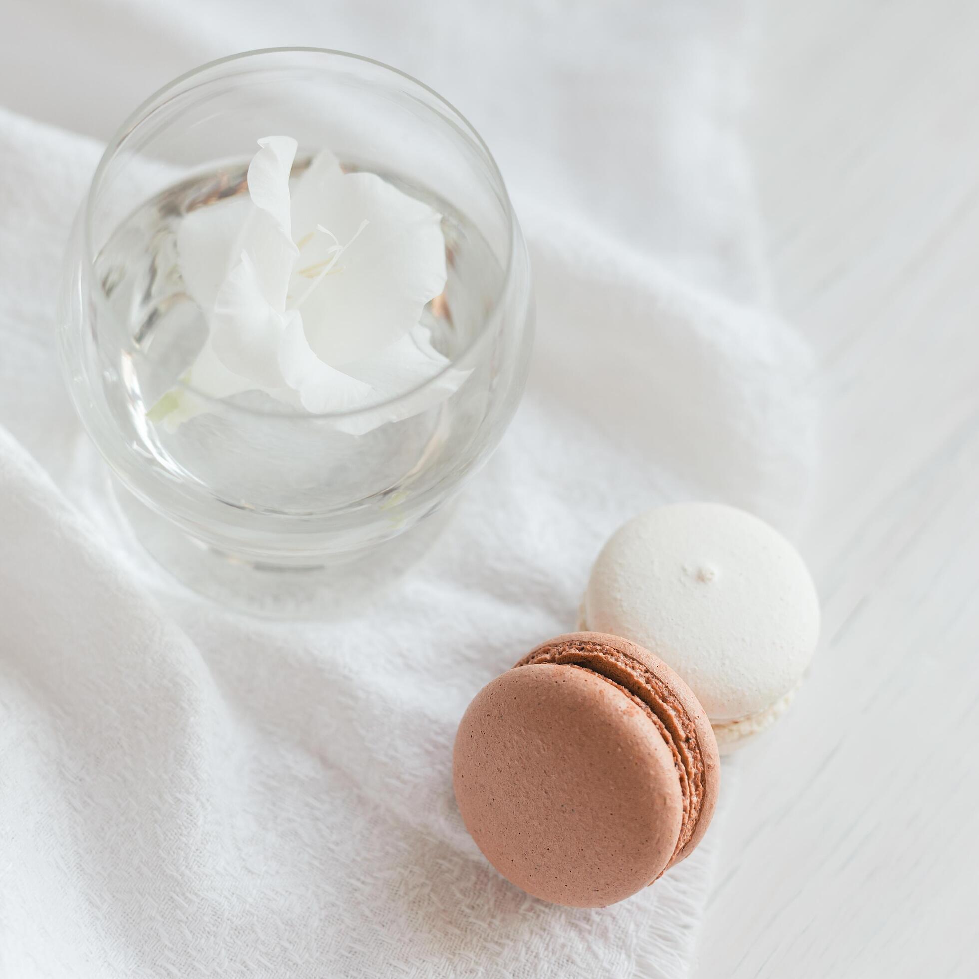 Two pastel French macarons and glass with flower on a white background. Stock Free