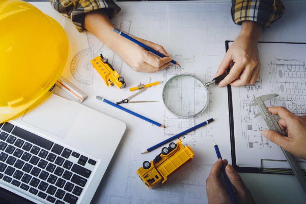 Two colleagues discussing data working and tablet, laptop with on on architectural project at construction site at desk in office Stock Free