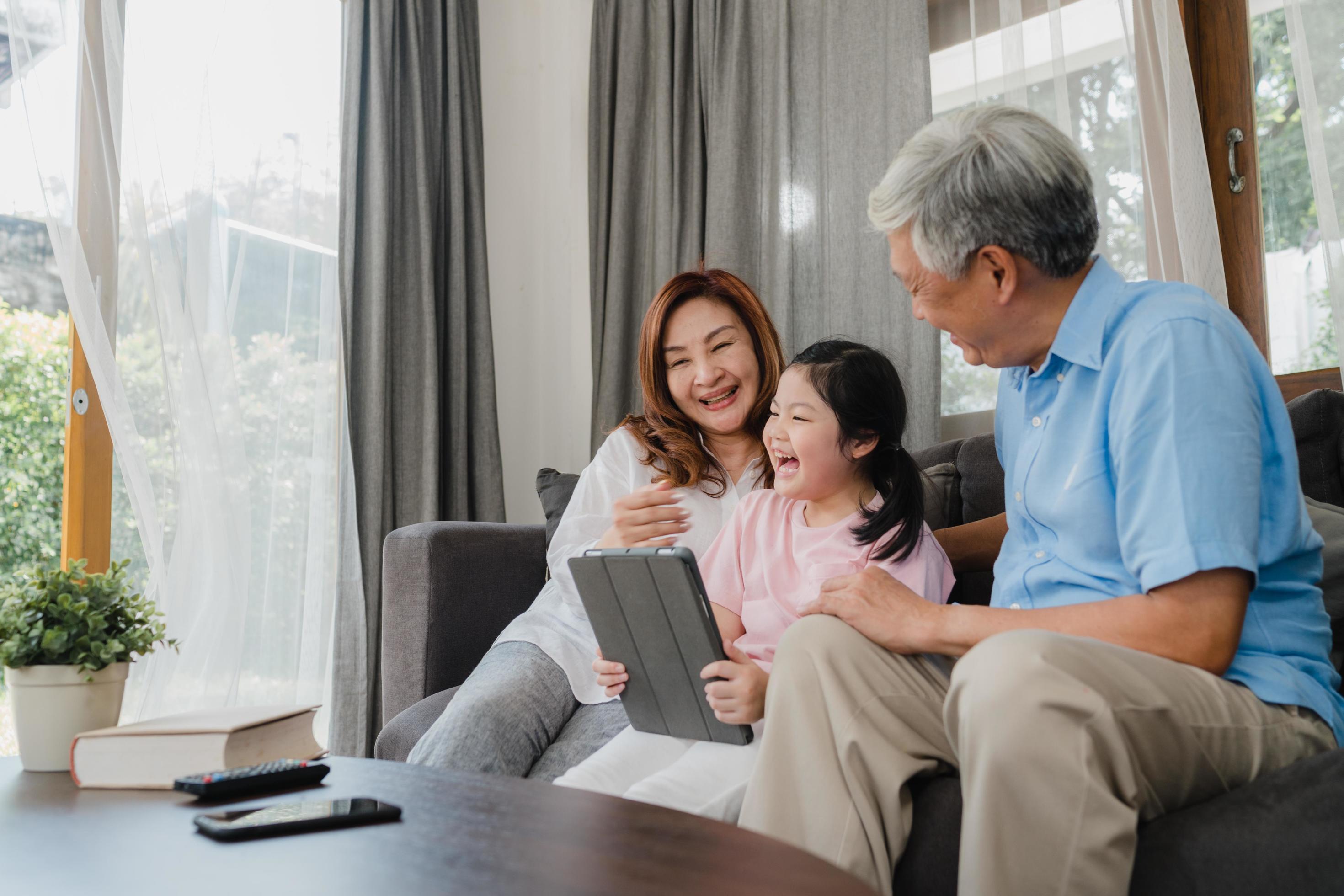 Asian grandparents and granddaughter using tablet at home Stock Free