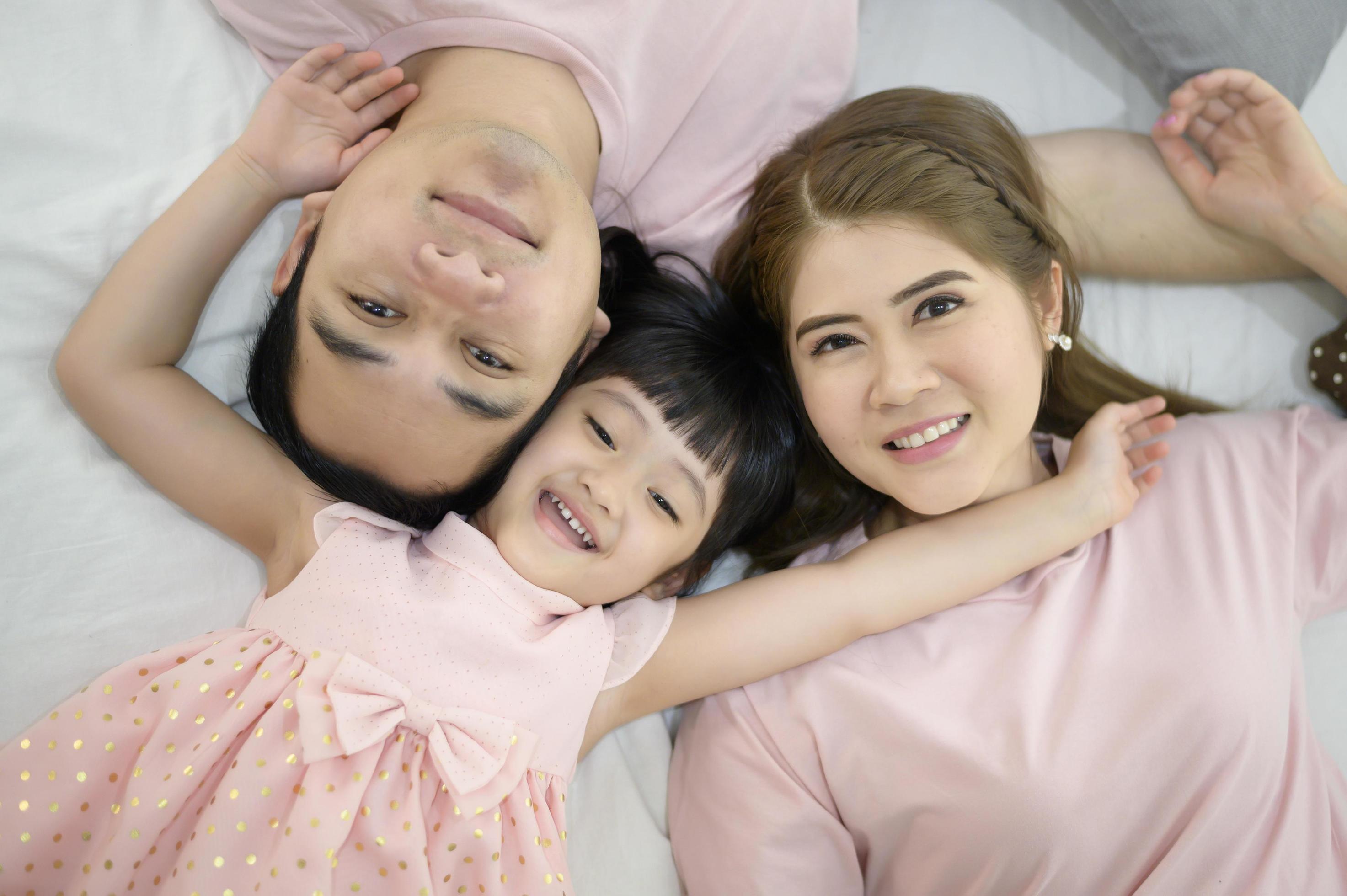 Top view of a happy asian family wearing pink shirt portrait on white bed indoor Stock Free