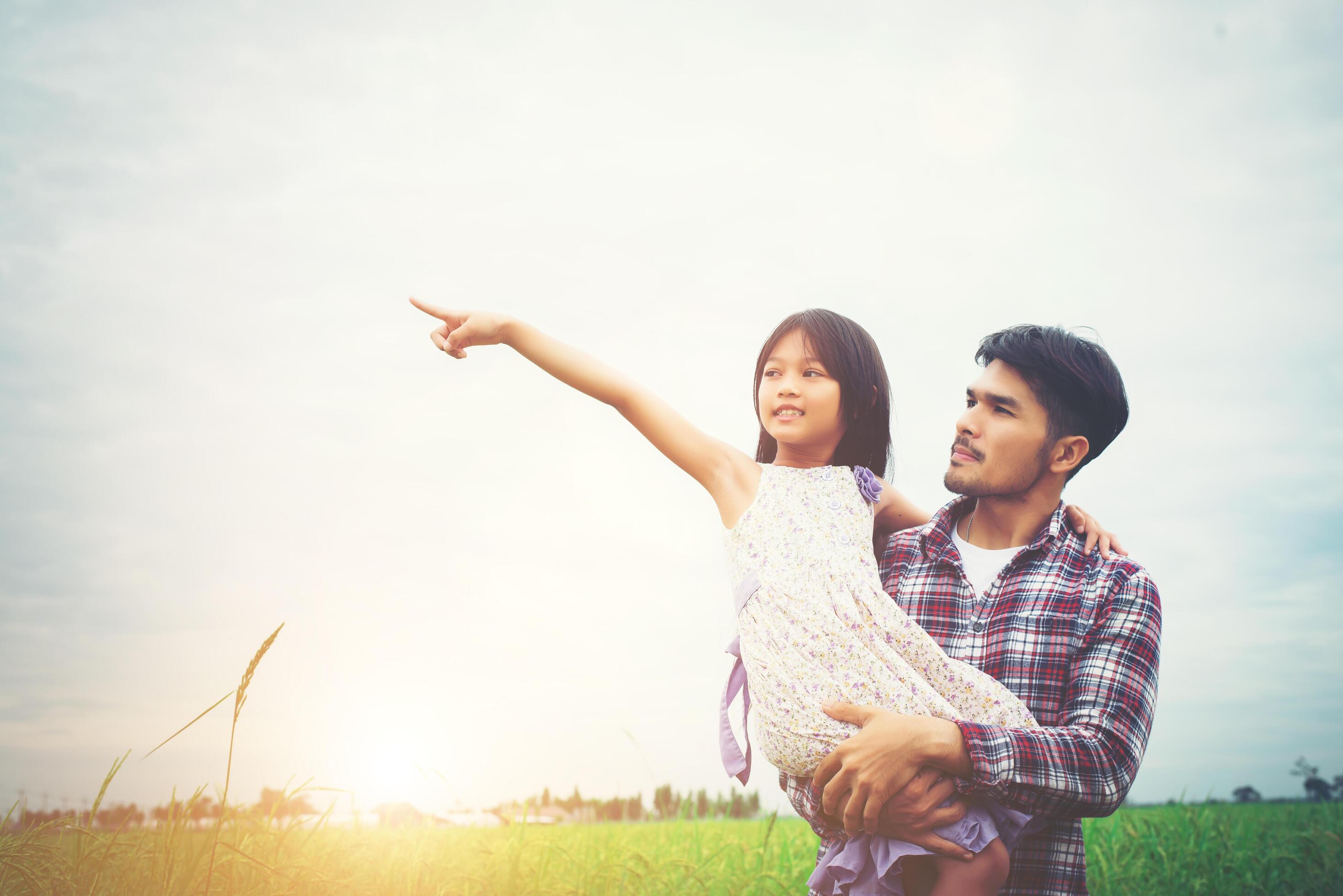 Daughter pointing away and smiling with her dad in the meadows field. Stock Free