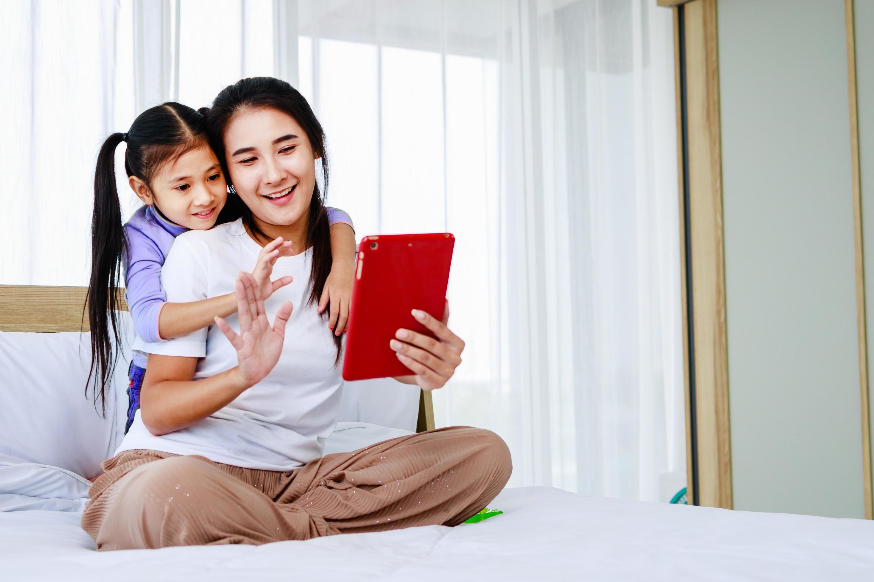 Happy mother with little girl are making selfie or video call to father or relatives in Bed Stock Free