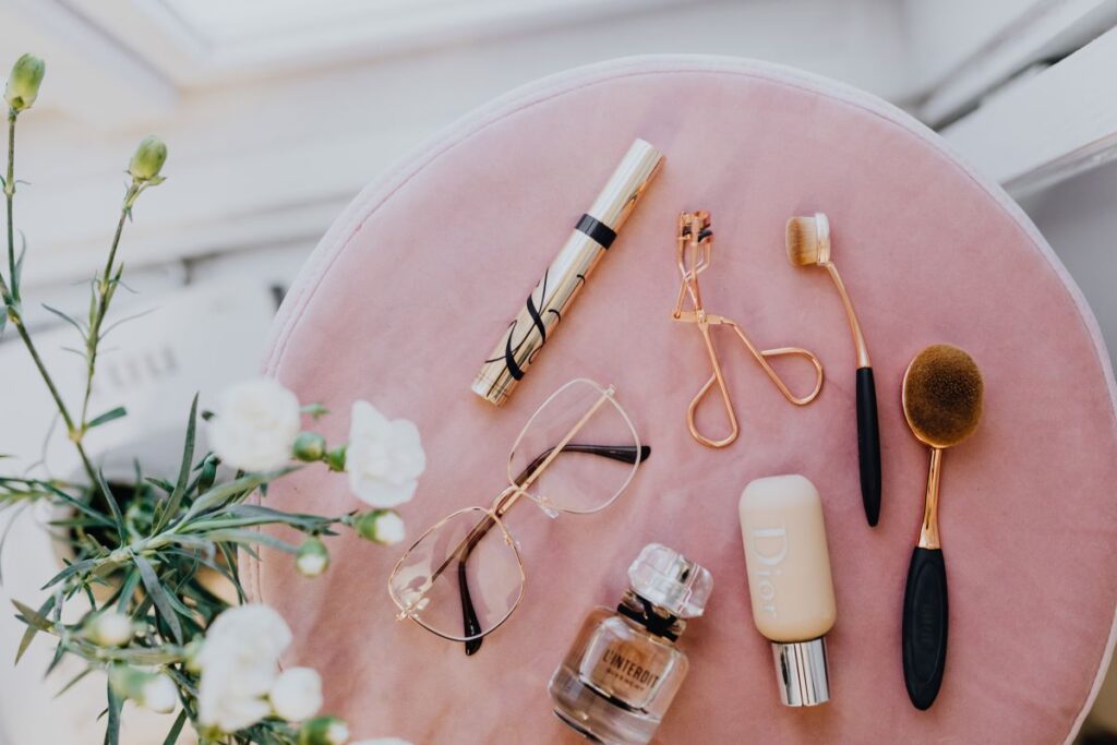 Makeup brushes, eyelash curler & a bottle of perfume on pink velvet Stock Free