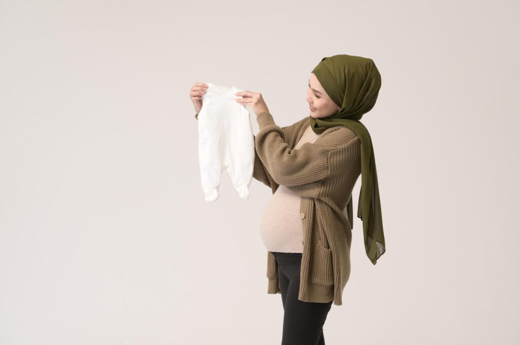 Portrait of Pregnant muslim woman in hijab holding baby cloth over white background studio Stock Free