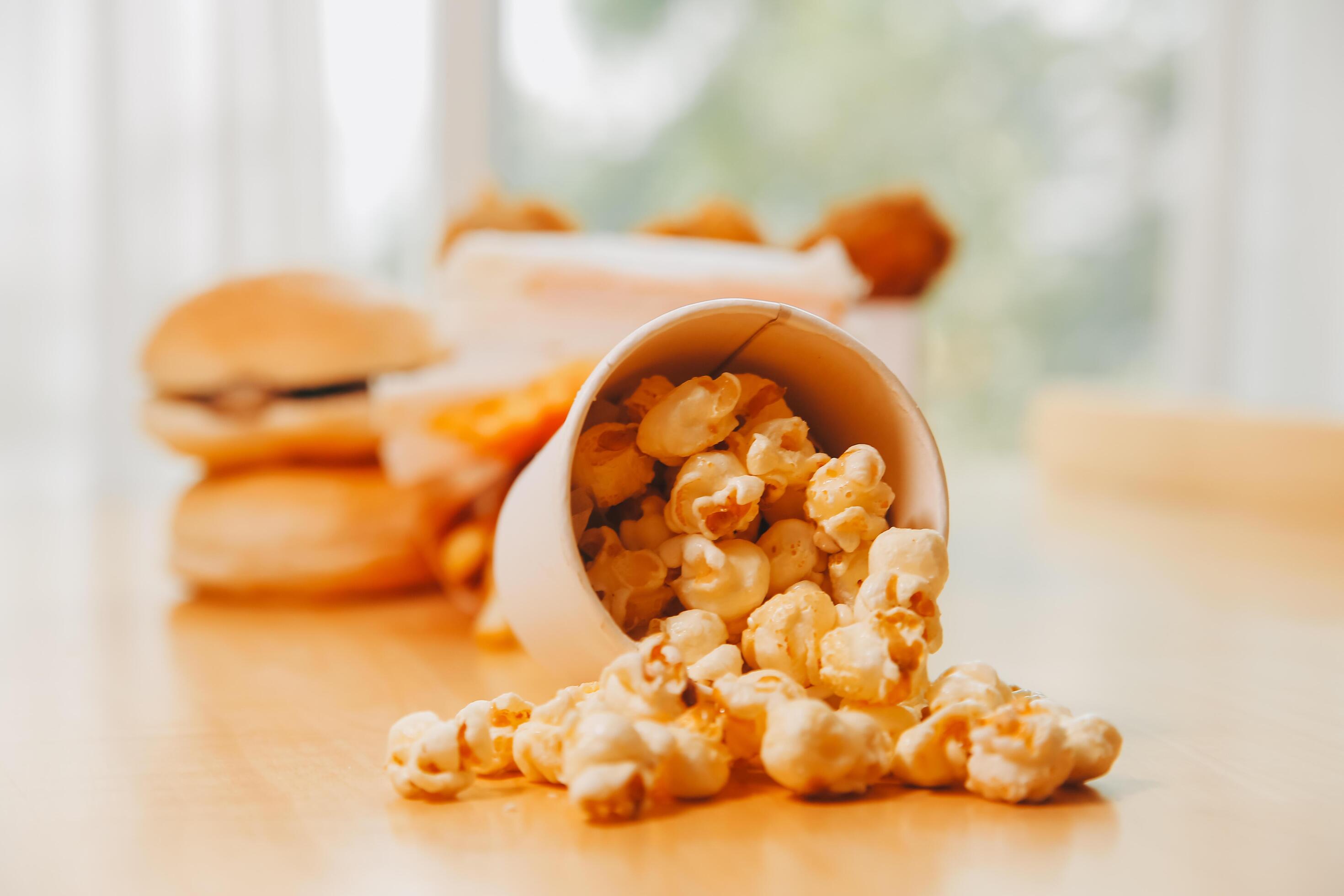 A bucket of popcorn, top-view, warm colors, light brown wooden background, flat lay, daylight macro close-up Stock Free