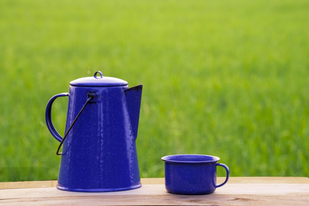 Kettle, blue enamel, and coffee mugs On an old wooden floor, Blurred background of rice fields at sunrise. Stock Free